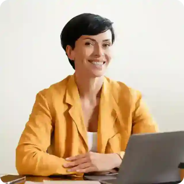 woman in yellow blazer smiling in front of a laptop