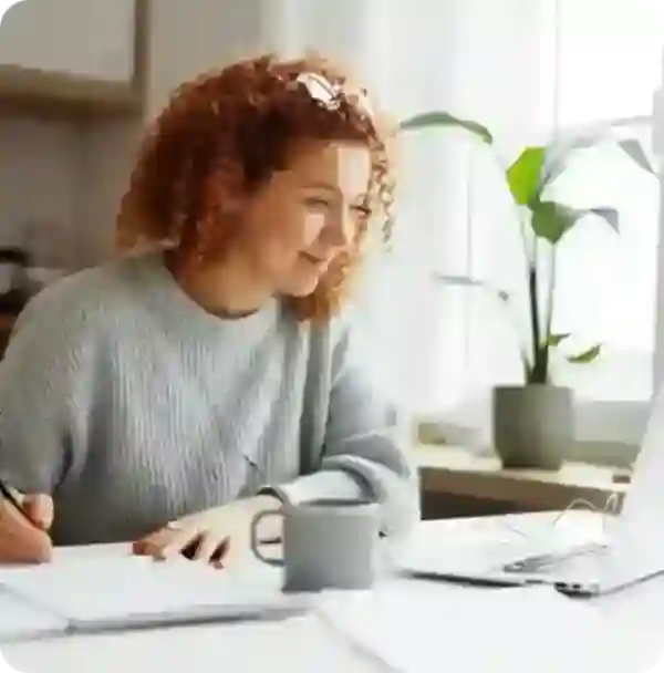 A girl smiling and looking at laptop while writing