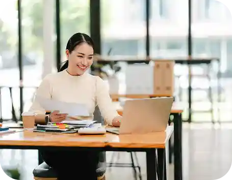 woman holding paperwork while working on a laptop
